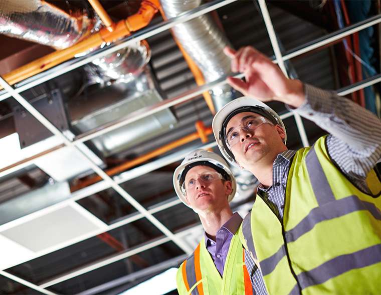 Two workers in safety equipment looking forward at pipes