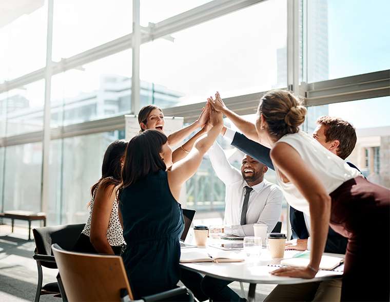 Office team members high fiving around the meeting table