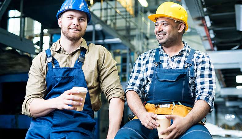 Two workers in hard hats enjoying a coffee