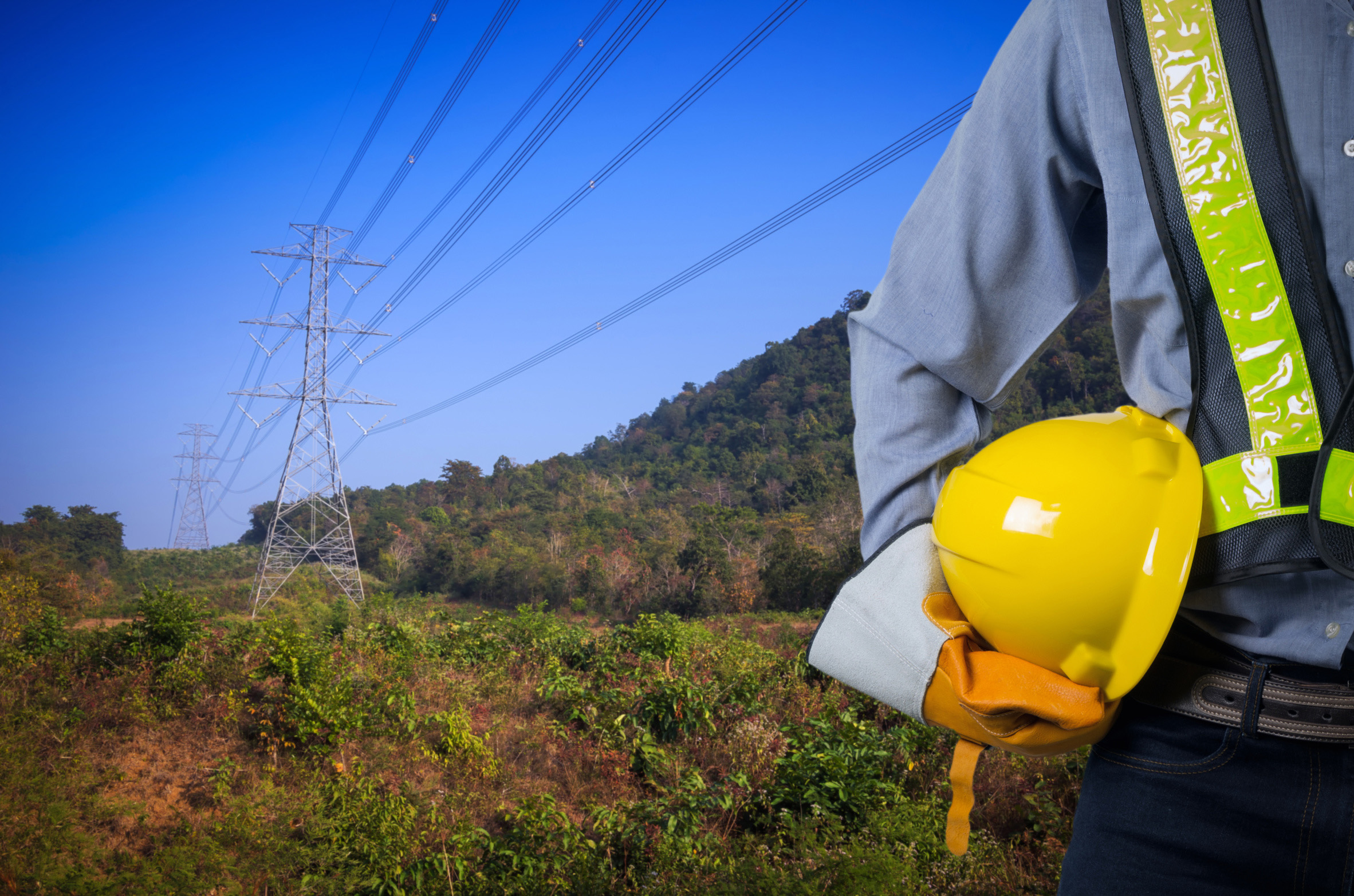 Person with yellow hard hat in front of hydro tower